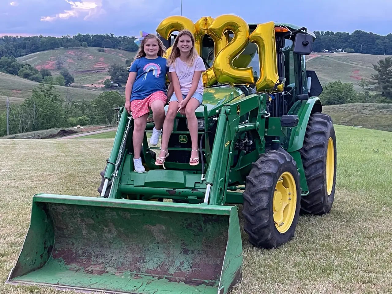Two girls sitting on a tractor with balloons