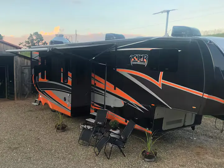 A black and orange rv parked in the sand.