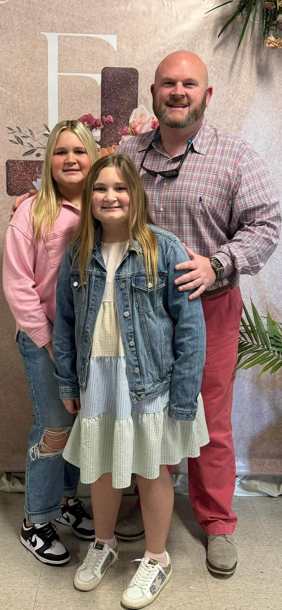 A girl standing between two men in front of a wall.
