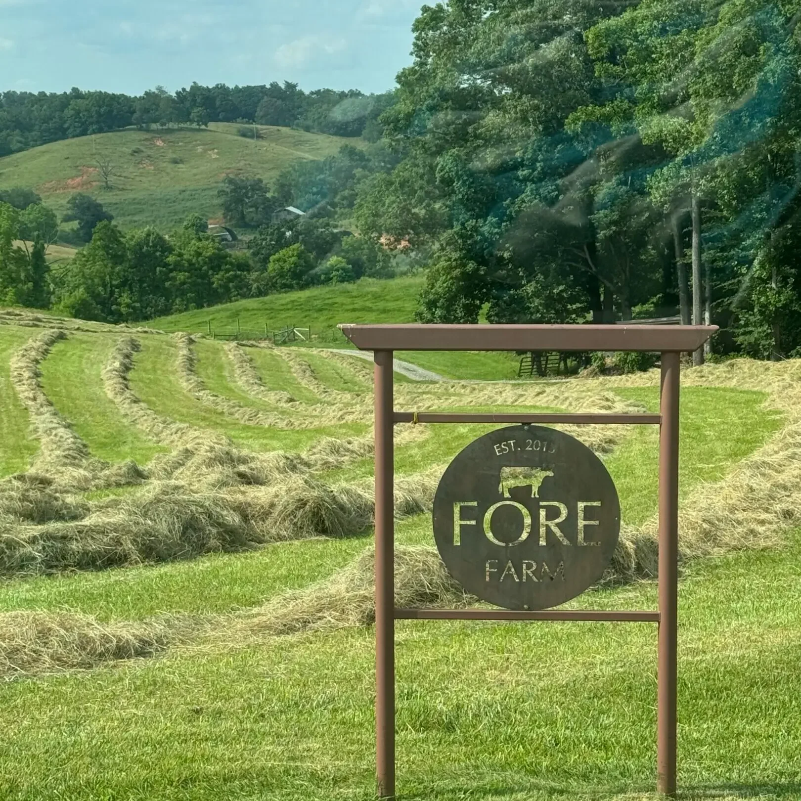 A sign in the middle of a field with trees and hills behind it.