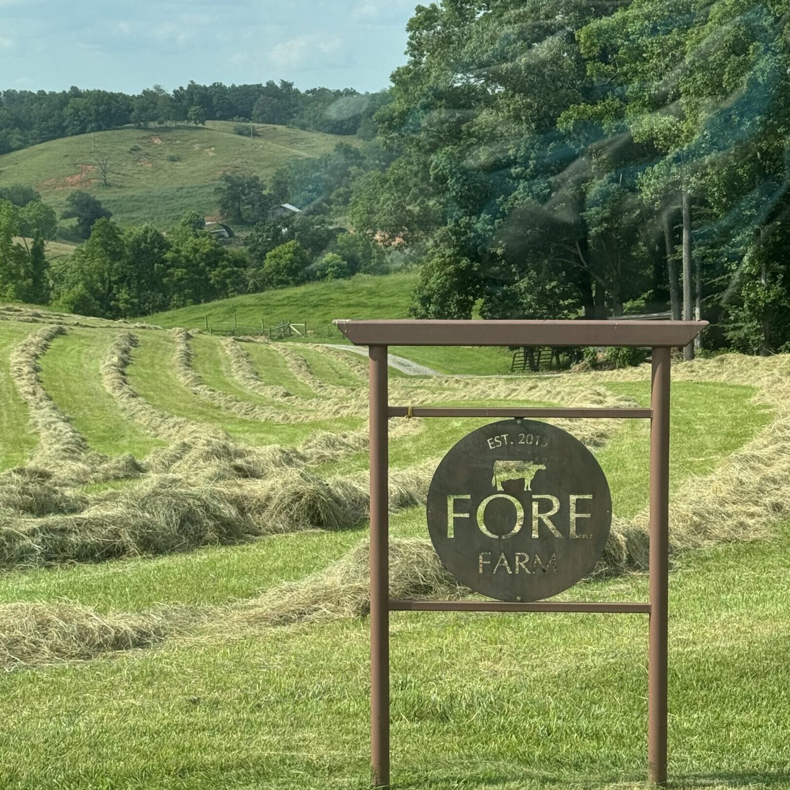 IMG_1528 A sign in the middle of a field with trees and hills behind it.
